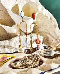 Surreal jewellery earrings featuring miniature utensils and fish hanging from a large white coral and ceramic oyster plate