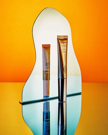 Cosmetic product tubes displayed on a reflective surface against a bright orange backdrop, creating a vibrant beauty product shot.