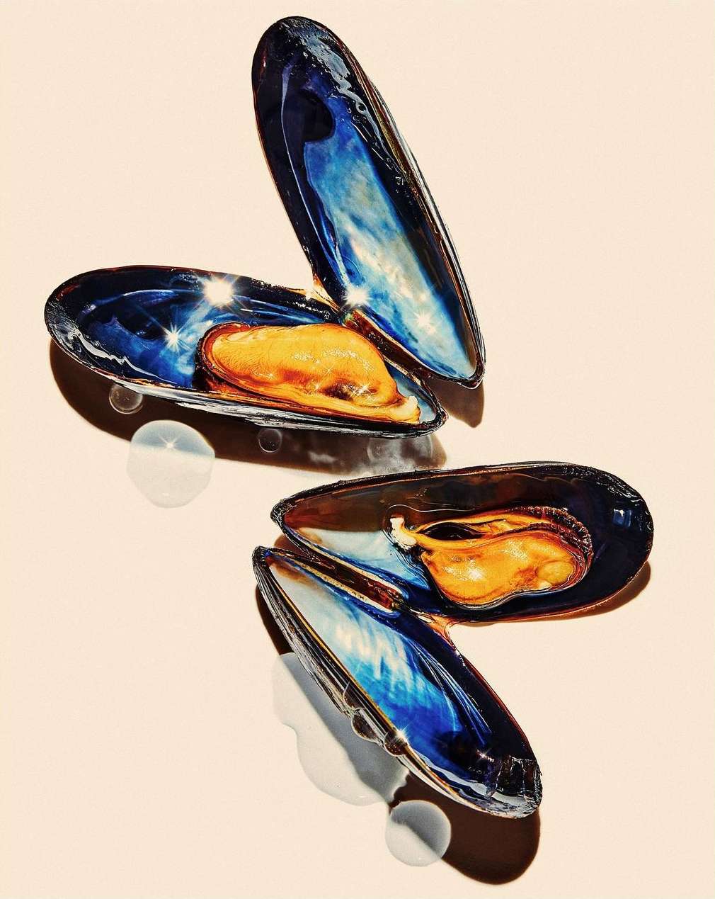 Two open mussels on a neutral backdrop showcasing their vibrant blue shells and orange interiors, captured in a visually appealing food still life.