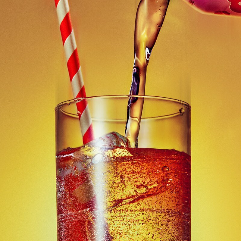 Iced drink being poured into a tall glass with a red and white striped straw on a yellow background; refreshment, beverage concept.