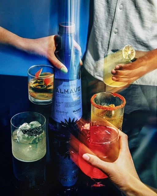A refreshing alcohol-free cocktail is prepared with Almave Blue Agave Spirit alternative and garnished with citrus on a dark surface.