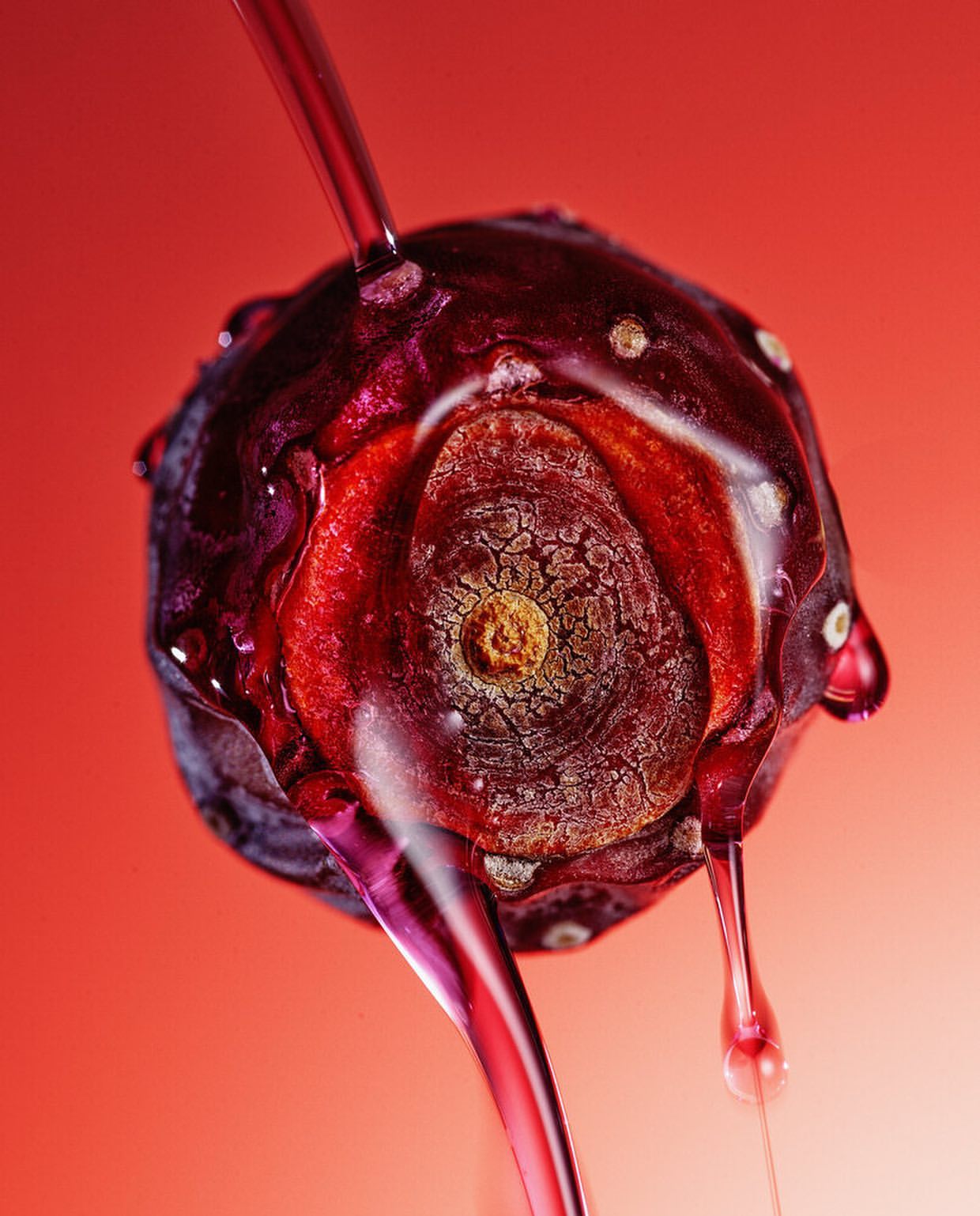 Macro shot of a half-cut plum with a juicy red interior, juice dripping, highlighting its texture against a warm red background.
