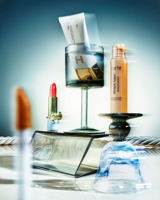 Hourglass, Tarte, and YSL beauty products arranged artfully on pedestals with blue background and diffused lighting for a product shoot.