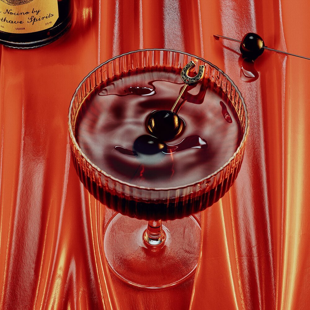 A stemmed cocktail glass filled with a dark red cocktail, garnished with cherries and a horseshoe pick on a shiny, orange background.