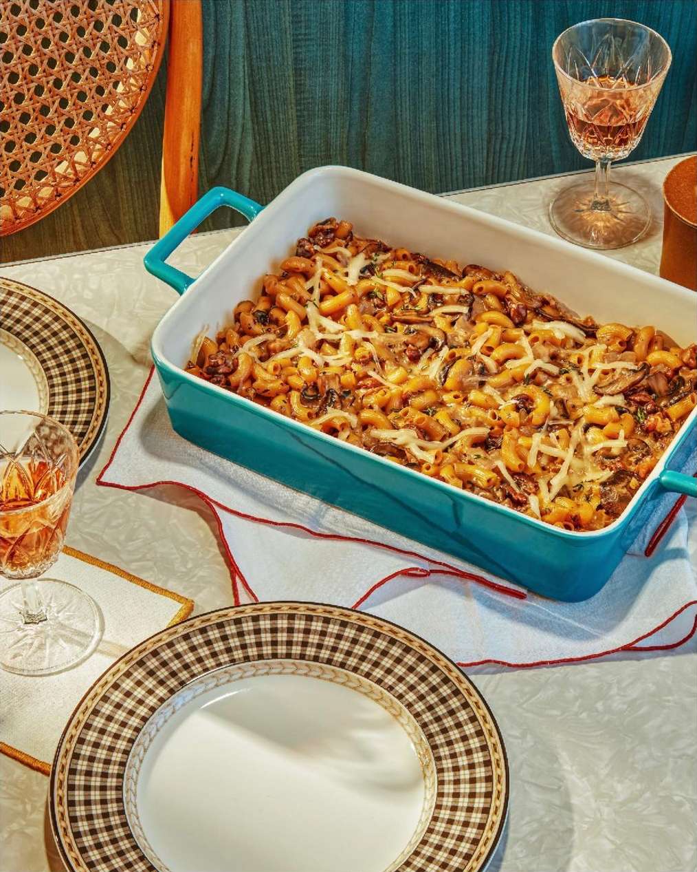 Overhead shot of baked pasta in a blue casserole dish, surrounded by plates, a glass, and table decor.