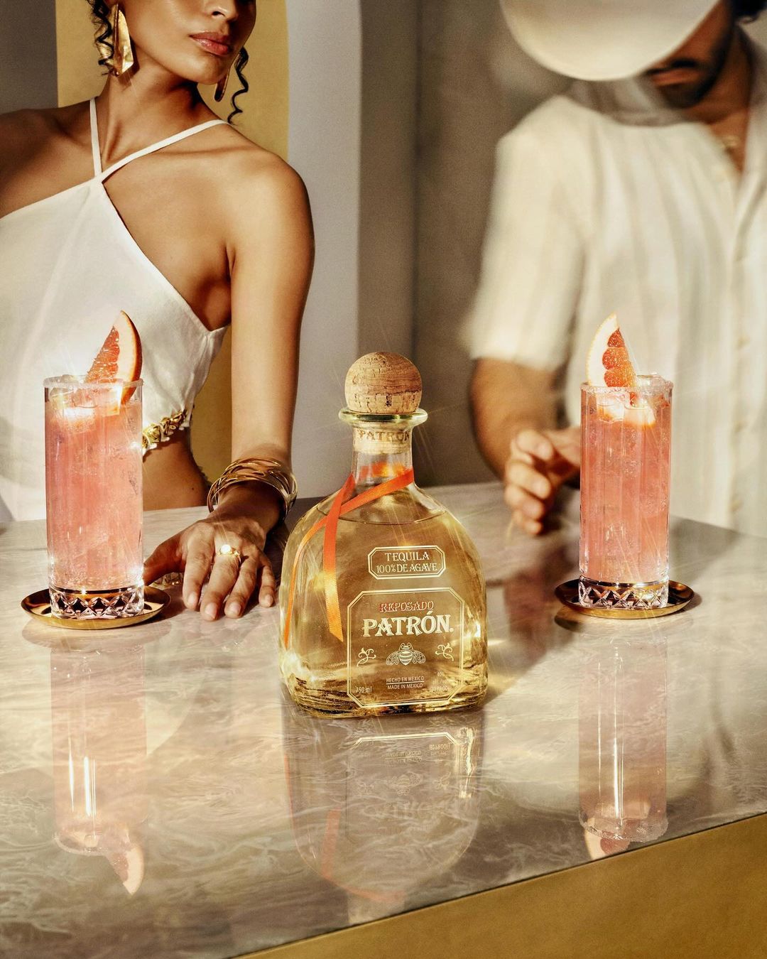 Tequila bottle on a marble bar top with two cocktails, one woman in white, and one man, product photography for food and beverage.