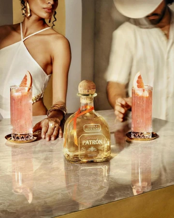 Tequila bottle on a marble bar top with two cocktails, one woman in white, and one man, product photography for food and beverage.