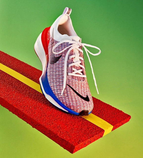 Close-up of a red, white, and blue Nike running shoe with white laces on a textured red platform against a bright green background.