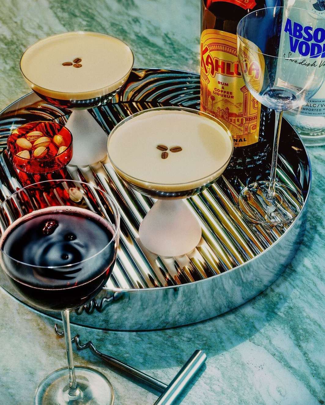 Two cocktails on a silver tray with liquor bottles and a wine glass, capturing a sophisticated and inviting beverage scene.