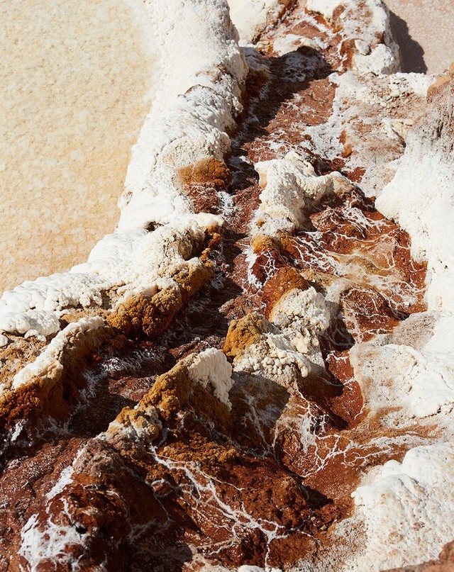 Aerial view of mineral formations featuring white crystalline deposits with red and brown hues, showcasing textures and patterns in nature.