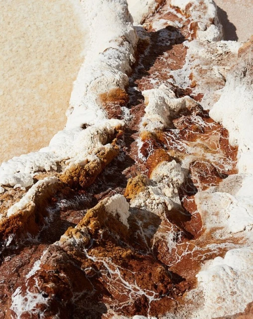 Aerial view of mineral formations featuring white crystalline deposits with red and brown hues, showcasing textures and patterns in nature.