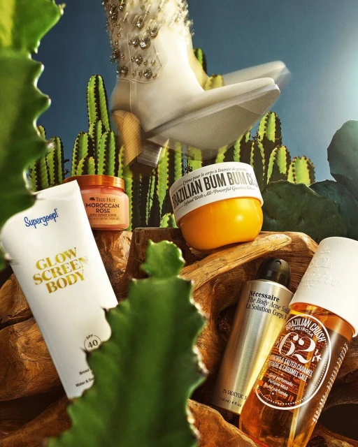 Close-up product still life featuring skincare products, a decorative cowboy boot, and cacti against a blue sky.