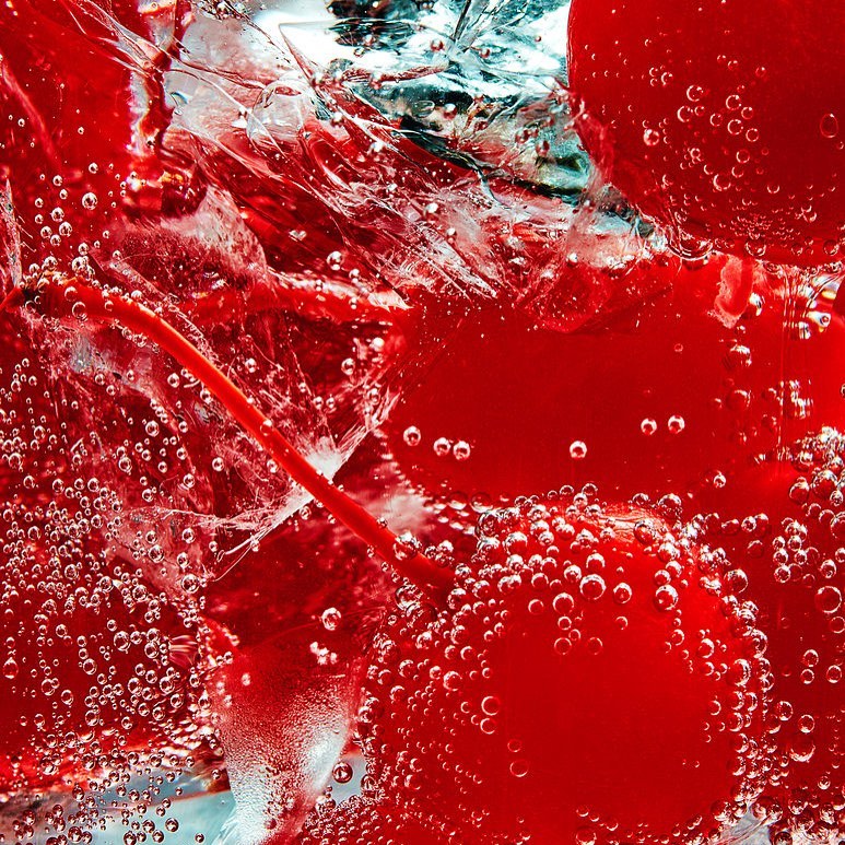 Close-up of bright red cherries suspended in bubbly water with ice creates refreshing, visually striking food and beverage aesthetic.