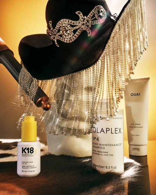 Hair product photography with a black cowboy hat, hair dryer, and product bottles on a faux cow skin background. 