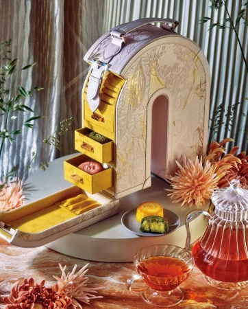 Luxurious gift box resembling a cabinet with mooncakes on a plate and a tea set, set against a backdrop of golden drapes and foliage.