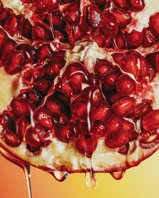 Close-up of a vibrant, halved pomegranate with glistening juice droplets, showcasing its intricate seed structure against a gradient background.