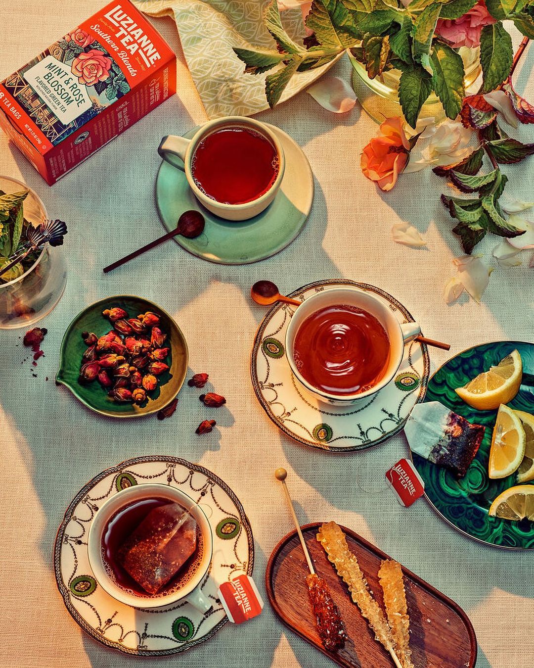 Overhead shot of tea cups, tea bags, sugar sticks, lemon slices, and rose hips arranged on a white tablecloth for a tea service.