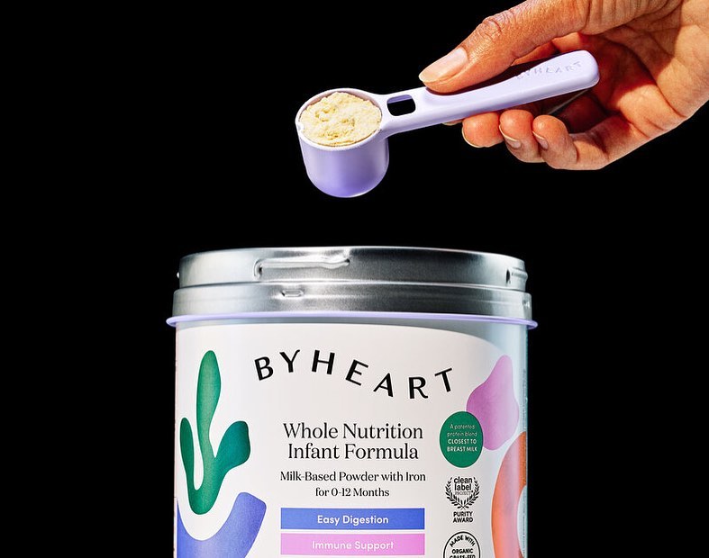 Infant formula can by ByHeart with a scoop of powder held above it. Infant nutrition for babies, with focus on nutrition and digestion.
