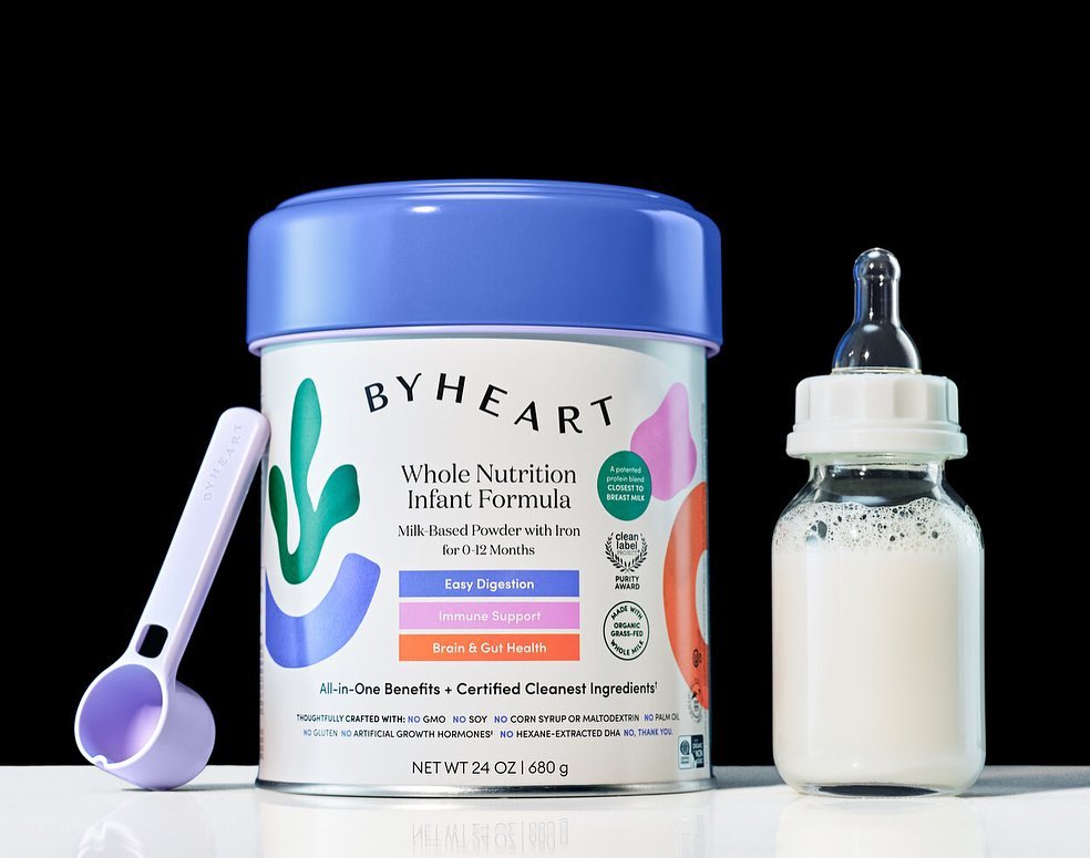 Infant formula can with feeding spoon and baby bottle against a black background for healthcare, food and beverage, or kids and family uses.