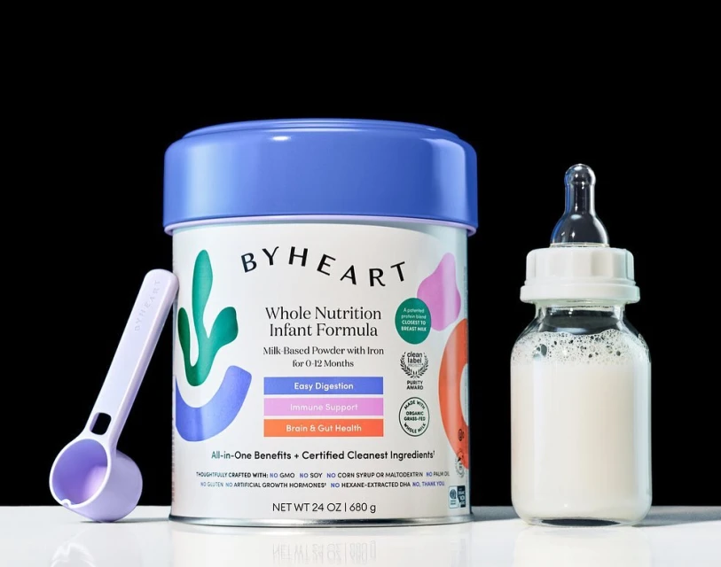 Infant formula can with feeding spoon and baby bottle against a black background for healthcare, food and beverage, or kids and family uses.