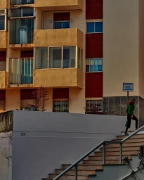 A person in a green top and dark trousers climbs concrete outdoor stairs beside an apartment building.