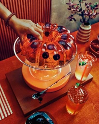 Close-up overhead shot of a hand touching a translucent red gelatin cake with cherries inside on a glass stand with two drinks on table