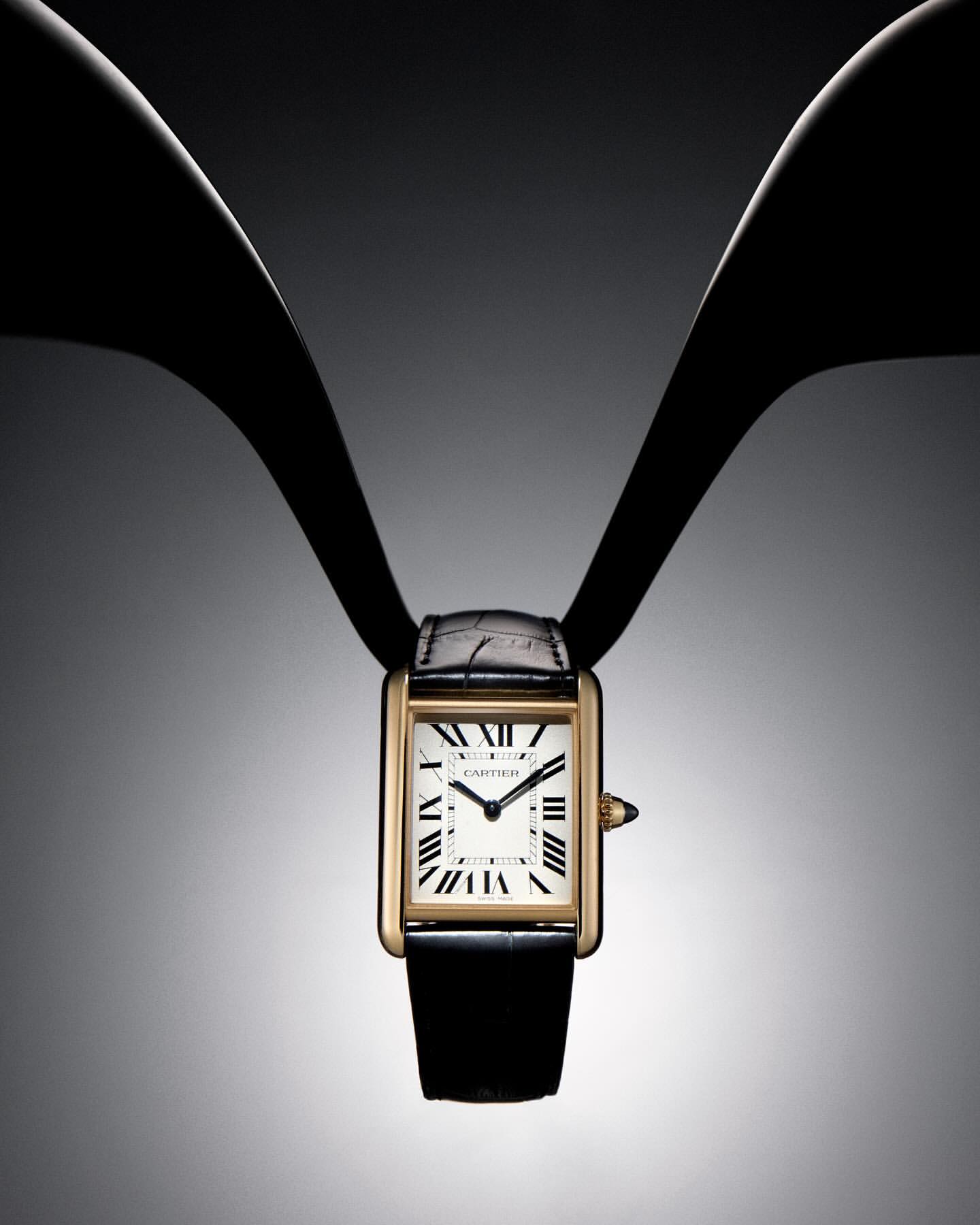 Elegant gold-tone wristwatch with a black leather strap is displayed on a graduated grey background with dark bands, fashion time.