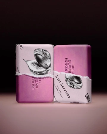 Two bars of fig-scented exfoliating soap with torn paper labels in a soft studio light against a dark mauve and gradient taupe background.