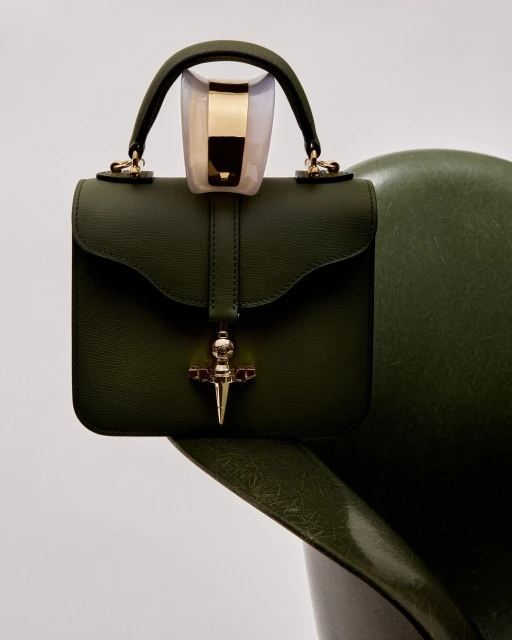Elegant olive green leather handbag on a matching chair against a plain white backdrop, capturing a high-fashion studio aesthetic.