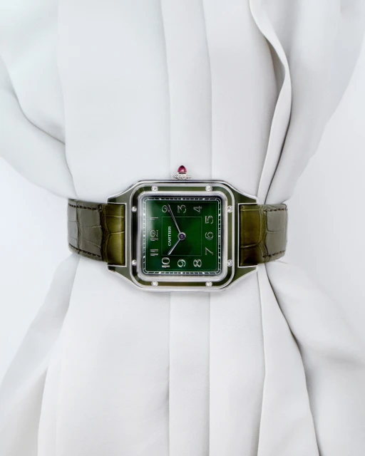 Close-up studio shot of a Cartier watch with a green face and alligator strap displayed on a white, draped garment.