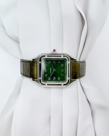 Close-up studio shot of a Cartier watch with a green face and alligator strap displayed on a white, draped garment.