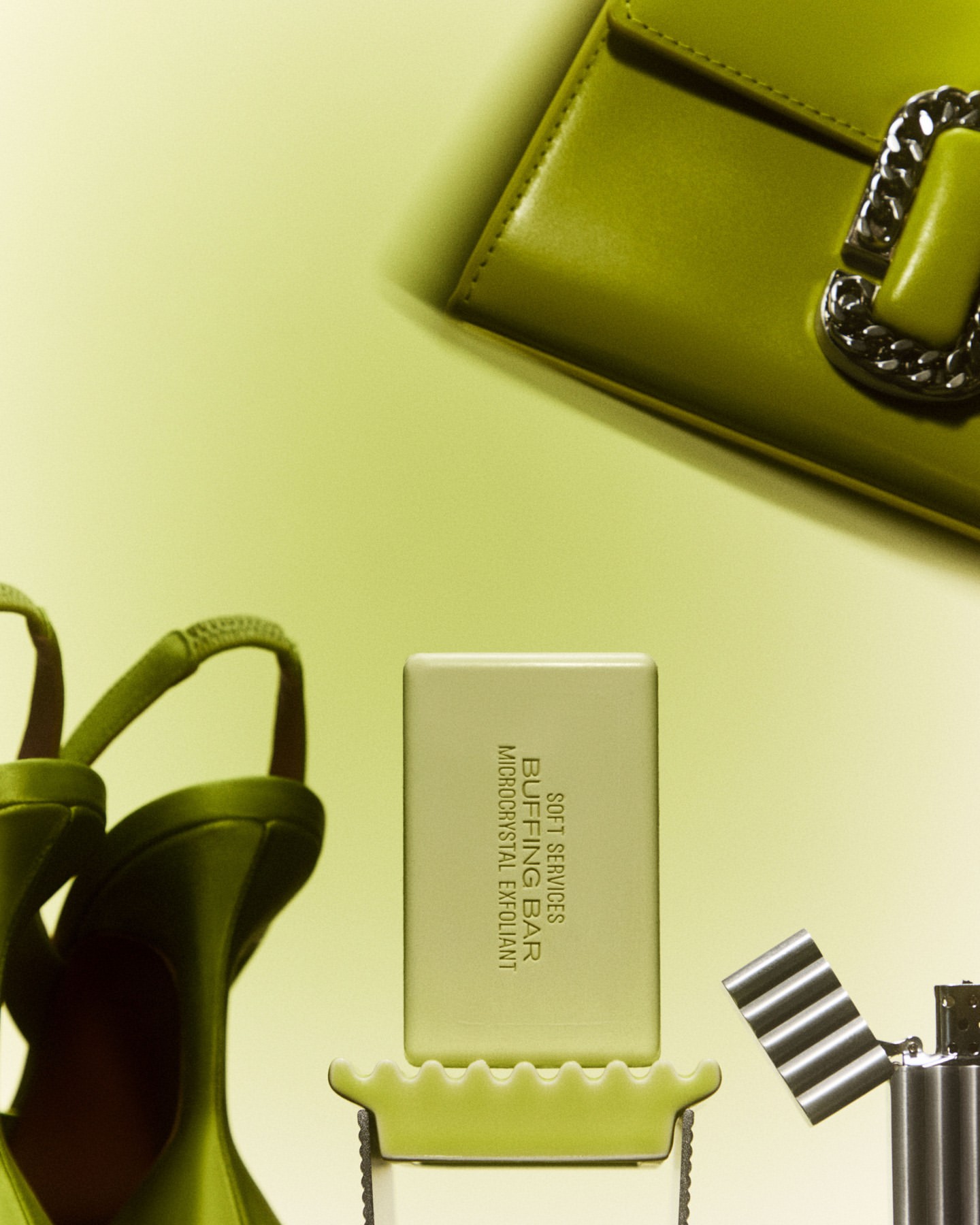 Still life shot of a bar of soap, shoes, handbag, and lighter against a pale yellow background. Products staged for commercial use.