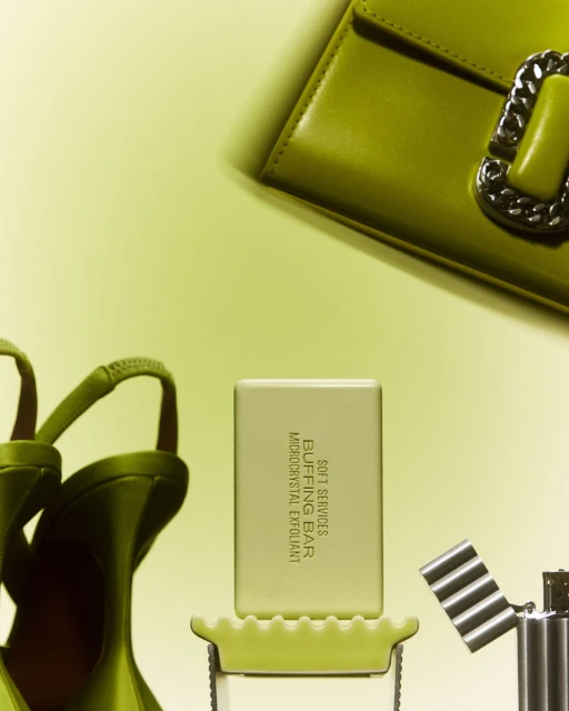 Still life shot of a bar of soap, shoes, handbag, and lighter against a pale yellow background. Products staged for commercial use.
