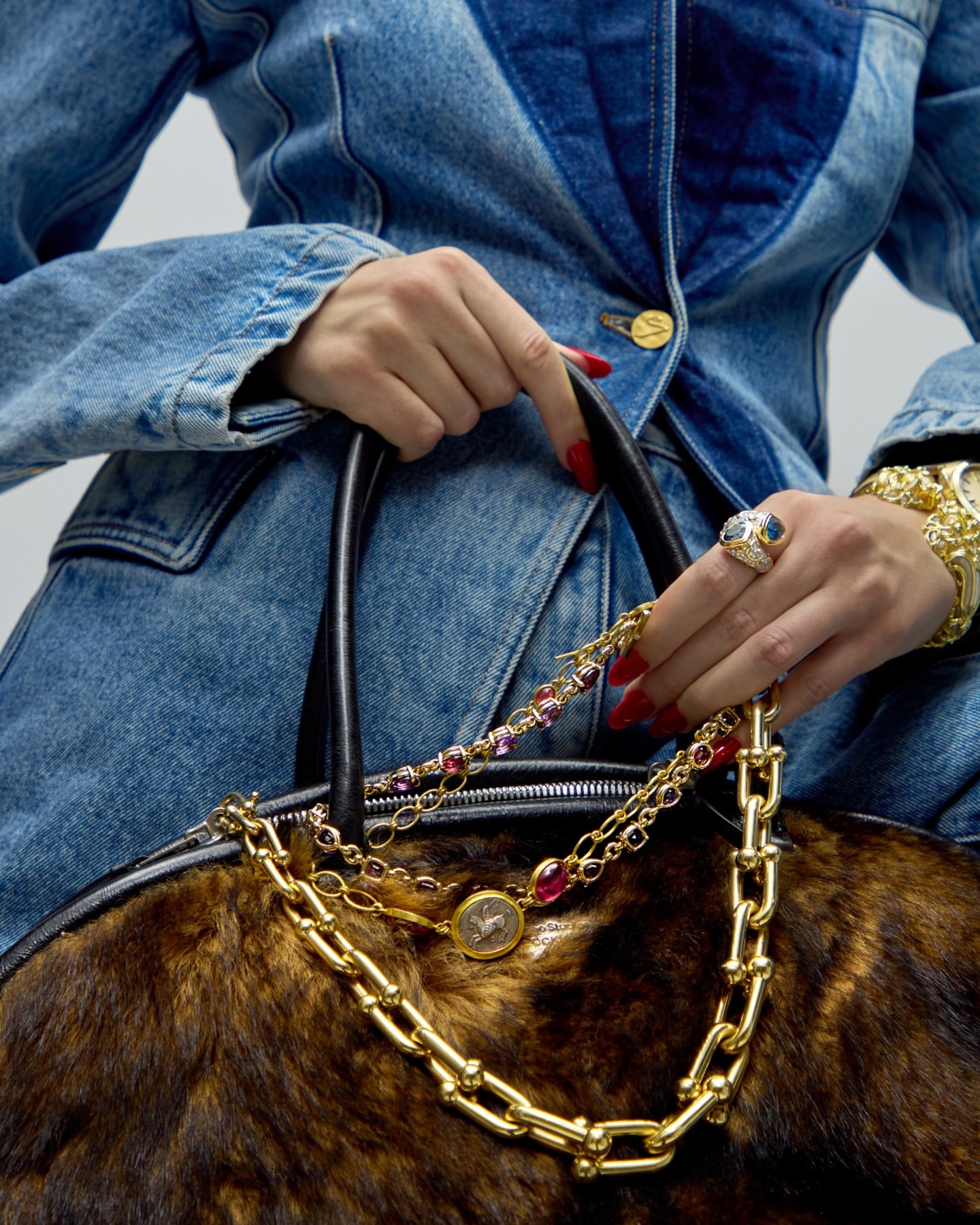 Close-up on a woman in a denim jacket holding a fur handbag, adorned with gold chains and jewelry, showcasing a fashion-forward style.