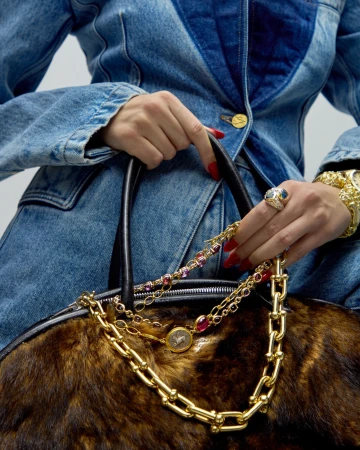 Close-up on a woman in a denim jacket holding a fur handbag, adorned with gold chains and jewelry, showcasing a fashion-forward style.