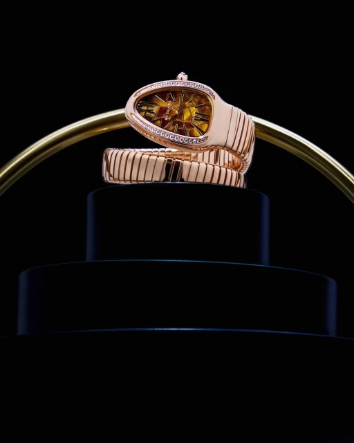 Rose gold Serpenti watch on a pedestal with black background. Luxury timepiece features diamond accents and snake-inspired design.
