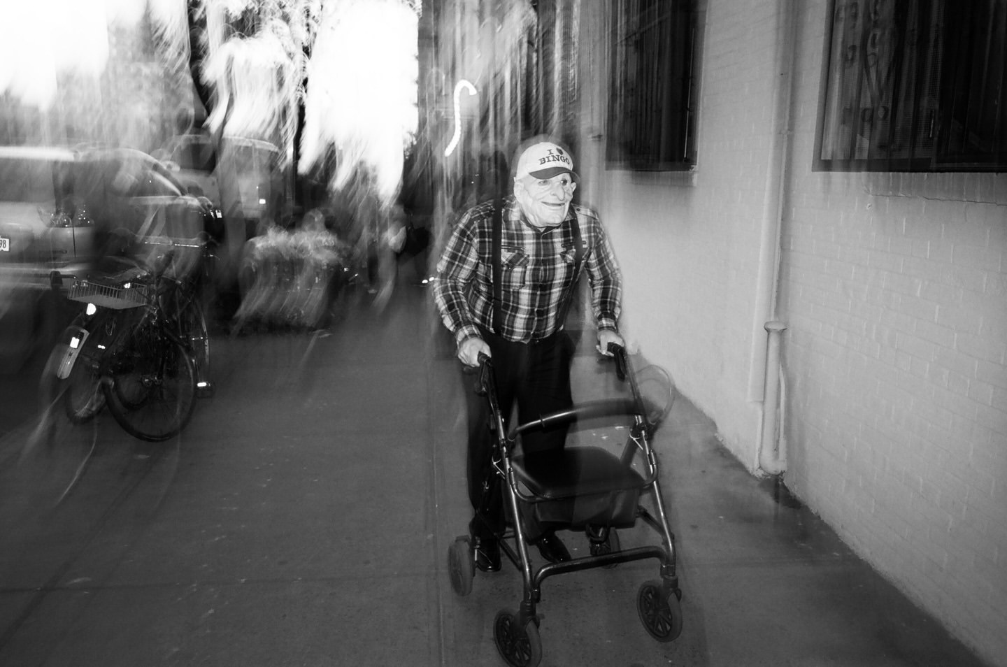 Monochrome image capturing an elderly man in a mask using a walker on a city street with a bike in background, creating a unique visual narrative.