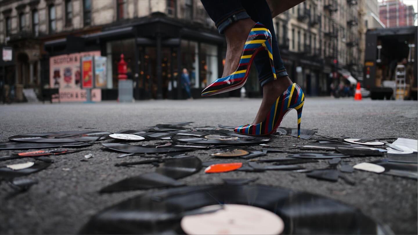 Striking image of a woman in striped heels walking on broken vinyl records in a city street, creating a visually arresting scene.