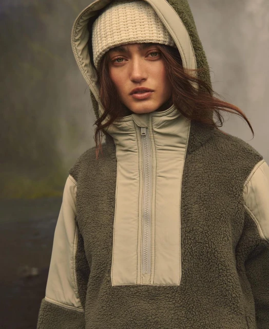 Woman wearing a green fleece pullover and cream-colored knit headband poses outdoors with a blurred, misty forest in the background.