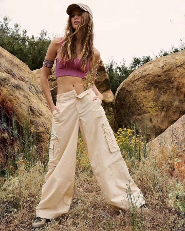 Model wearing a pink crop top and beige cargo pants standing outdoors amid rocky terrain and sparse vegetation.