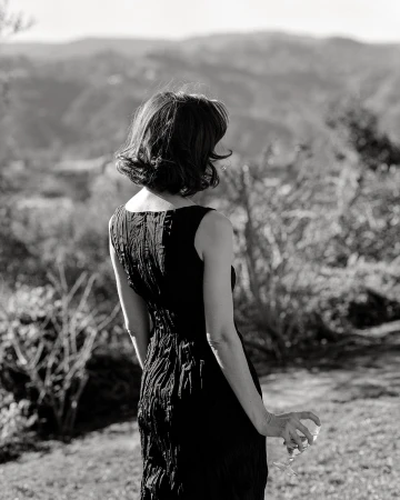 Woman in a black dress holding a wine glass outdoors with hills in the background, captured in monochrome by Chloe Chippendale.