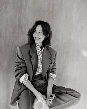 Black and white portrait of a smiling woman wearing an oversized tailored blazer and patterned shirt holding a small flower in Paris.