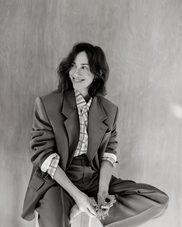 Black and white portrait of a smiling woman wearing an oversized tailored blazer and patterned shirt holding a small flower in Paris.