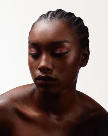 Close-up portrait of a Black woman with braided hair and pink eyeshadow against a plain white background