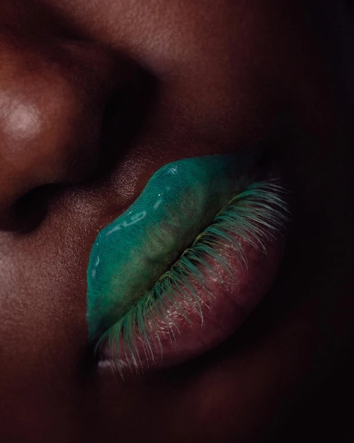 Close-up of a dark-skinned person's face with bright green, glossy lipstick enhancing the lips and partial view of their nose.