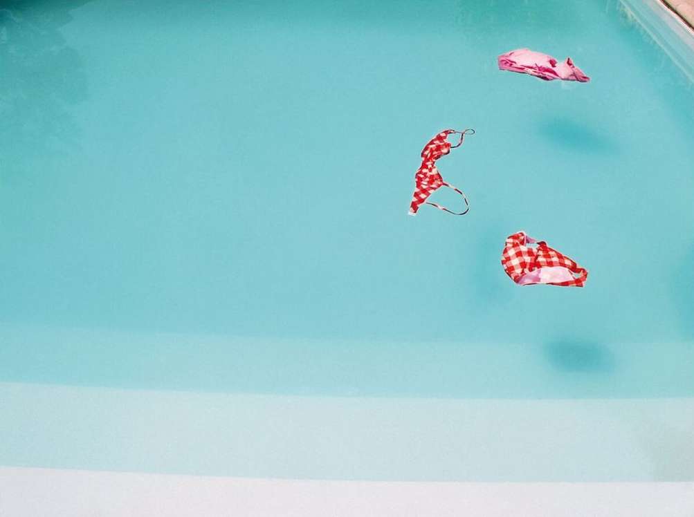 High-angle view of three women's bikini tops in a swimming pool with turquoise water on a sunny day, creating a vibrant and playful scene.