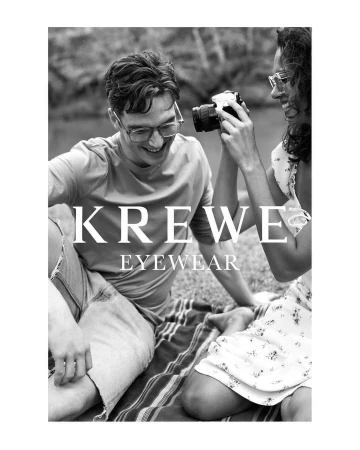 Black and white portrait of a man and woman smiling outdoors, with the woman holding up a vintage camera.