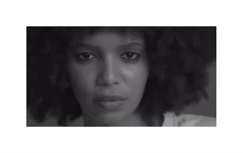 Close-up portrait of an adult female with dark skin and curly hair in a black and white photograph looking directly at the camera.