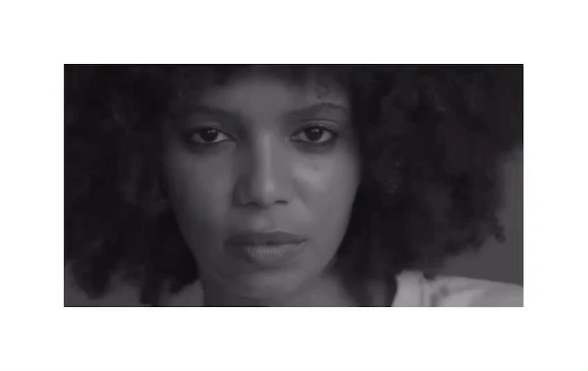 Close-up portrait of an adult female with dark skin and curly hair in a black and white photograph looking directly at the camera.