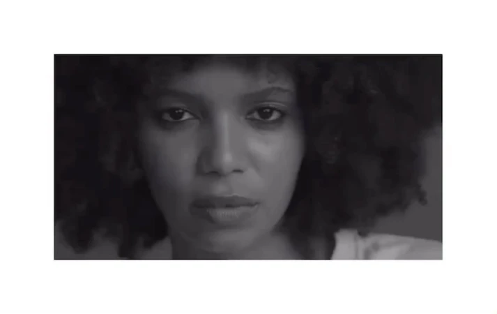Close-up portrait of an adult female with dark skin and curly hair in a black and white photograph looking directly at the camera.